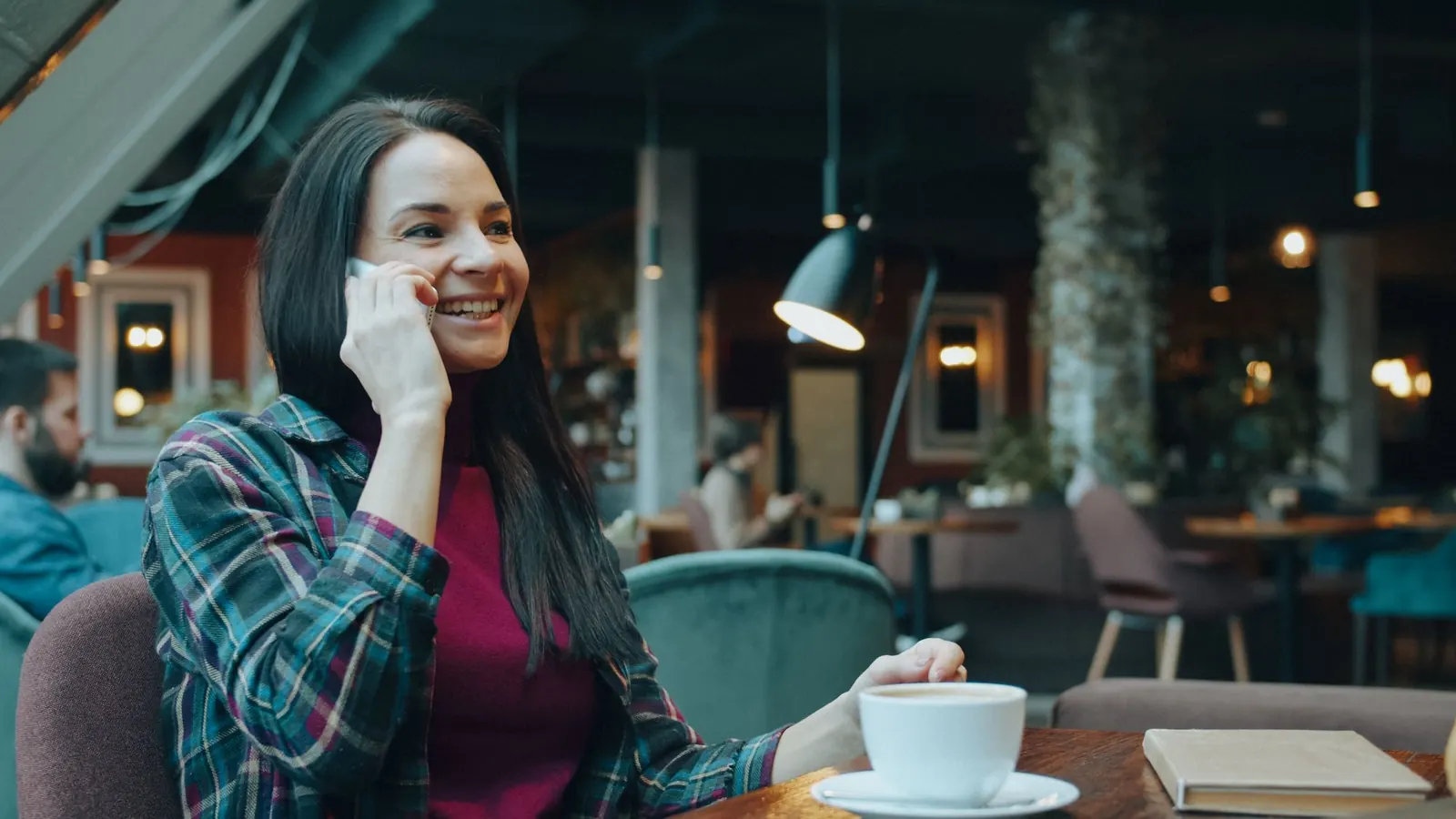 A woman smiling on her phone at a café table