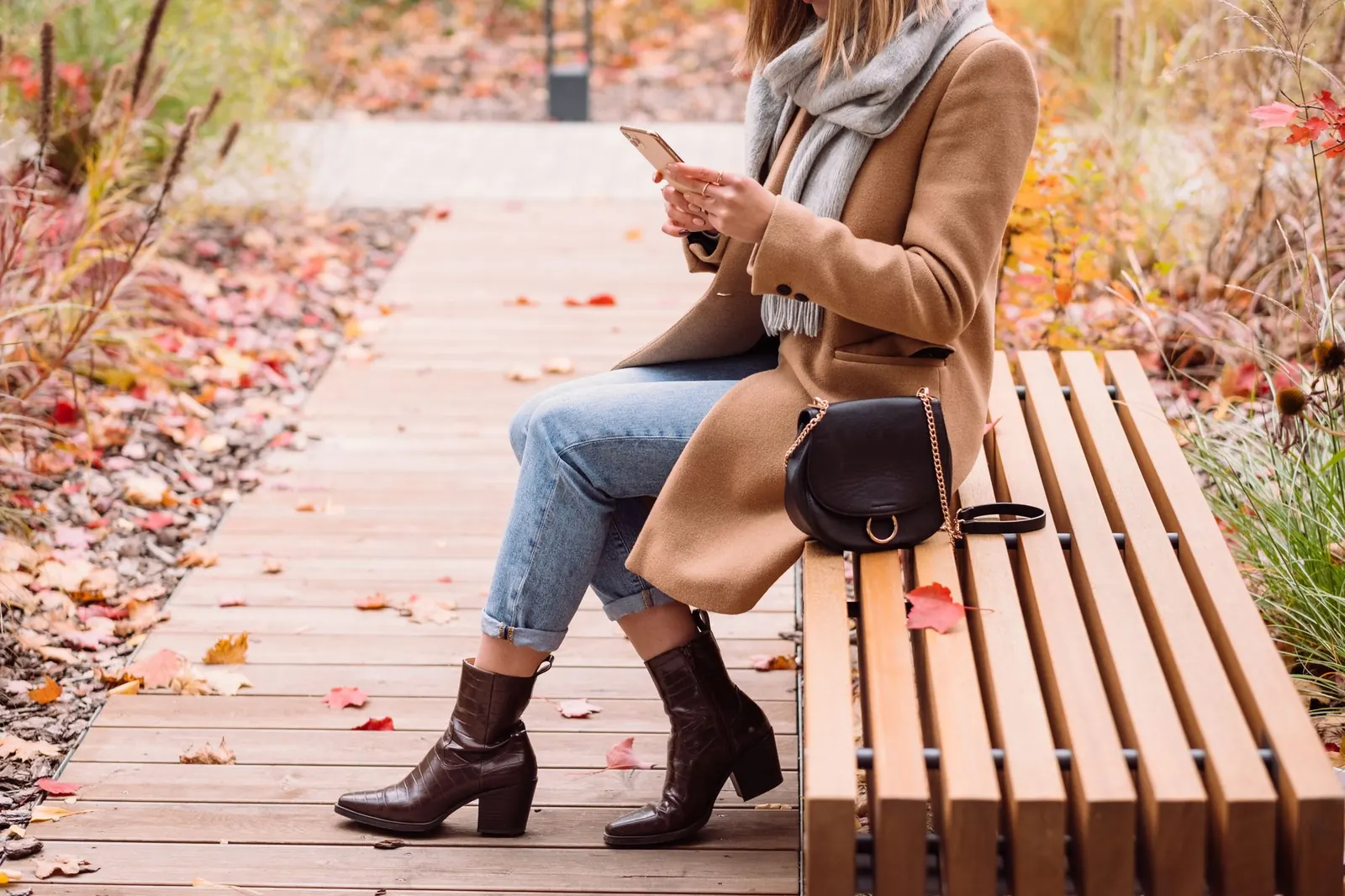 A woman on a park bench in autumn looking at her phone