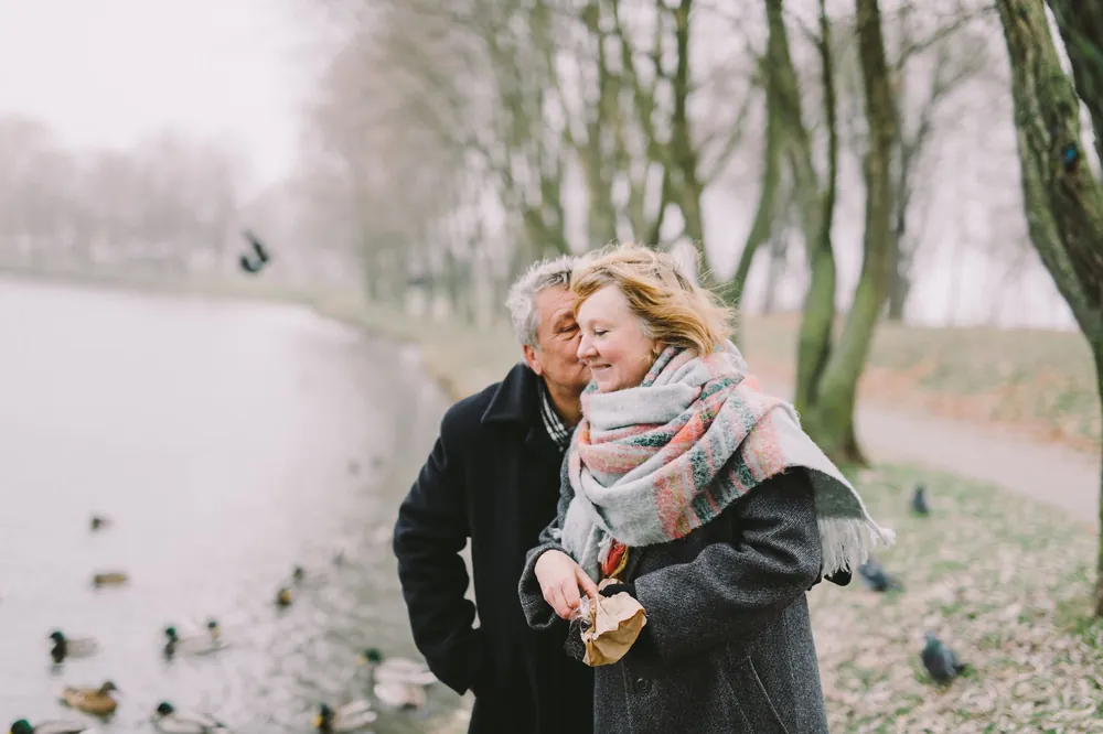 An older couple walking arm in arm by a lake in winter