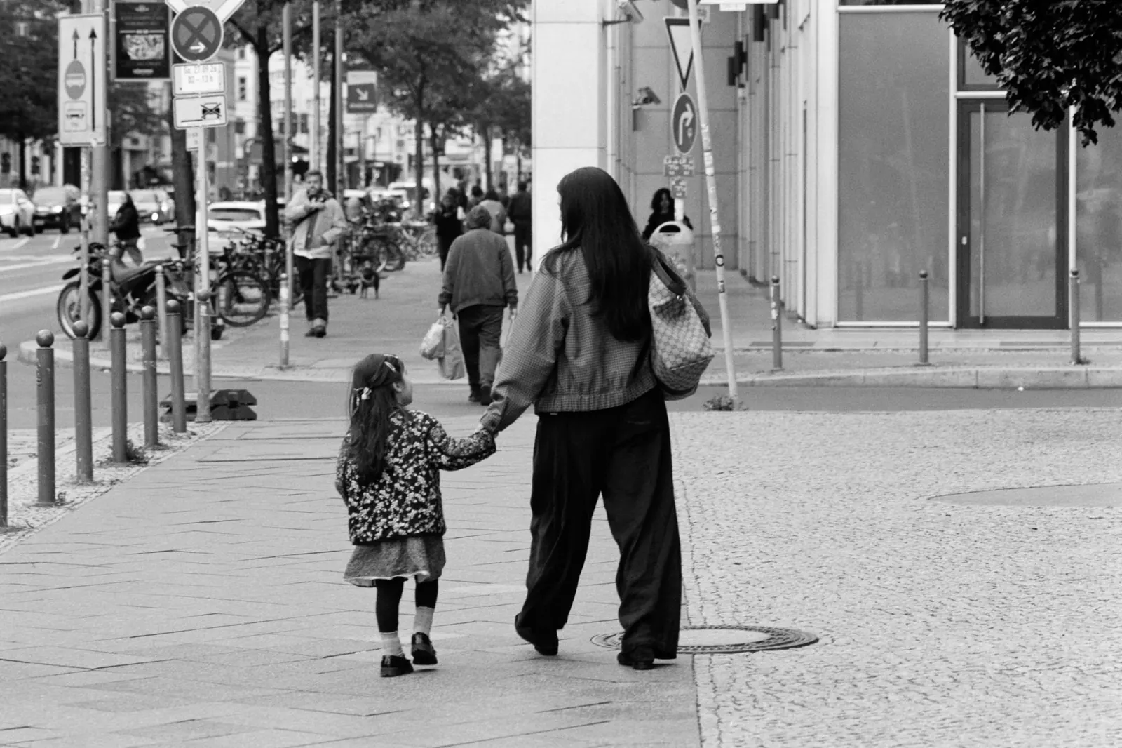 A mother and child walking hand in hand down a city street