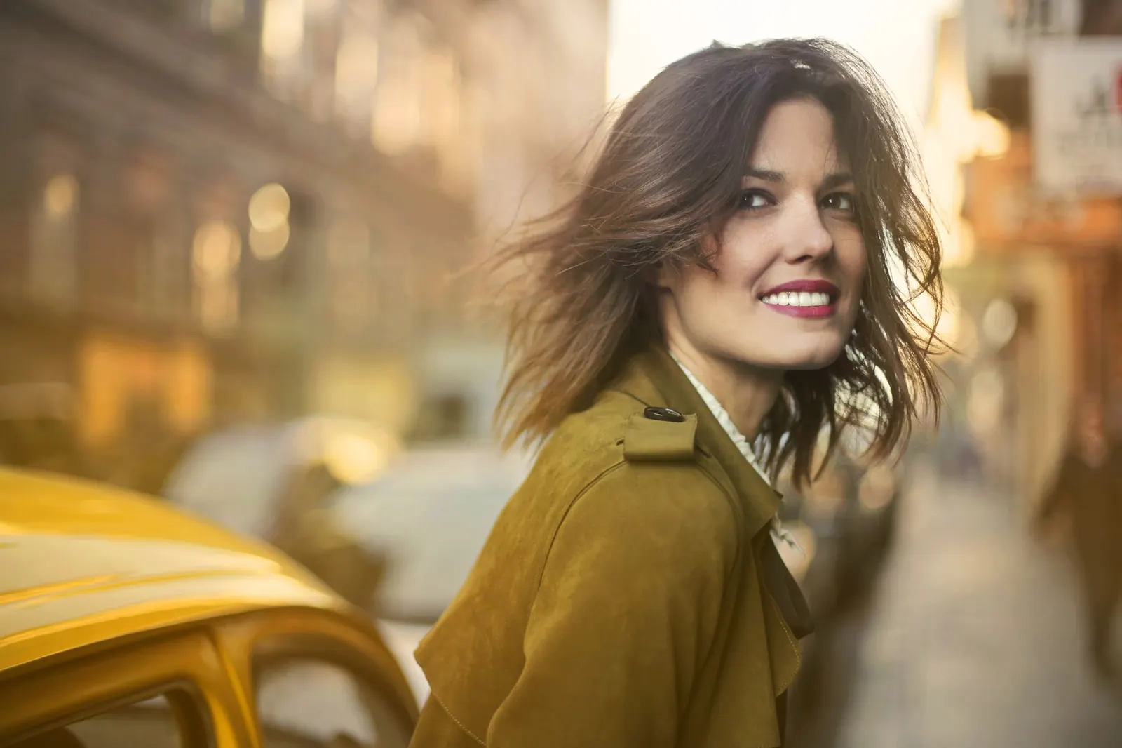 A smiling woman in a coat on a sunny city street