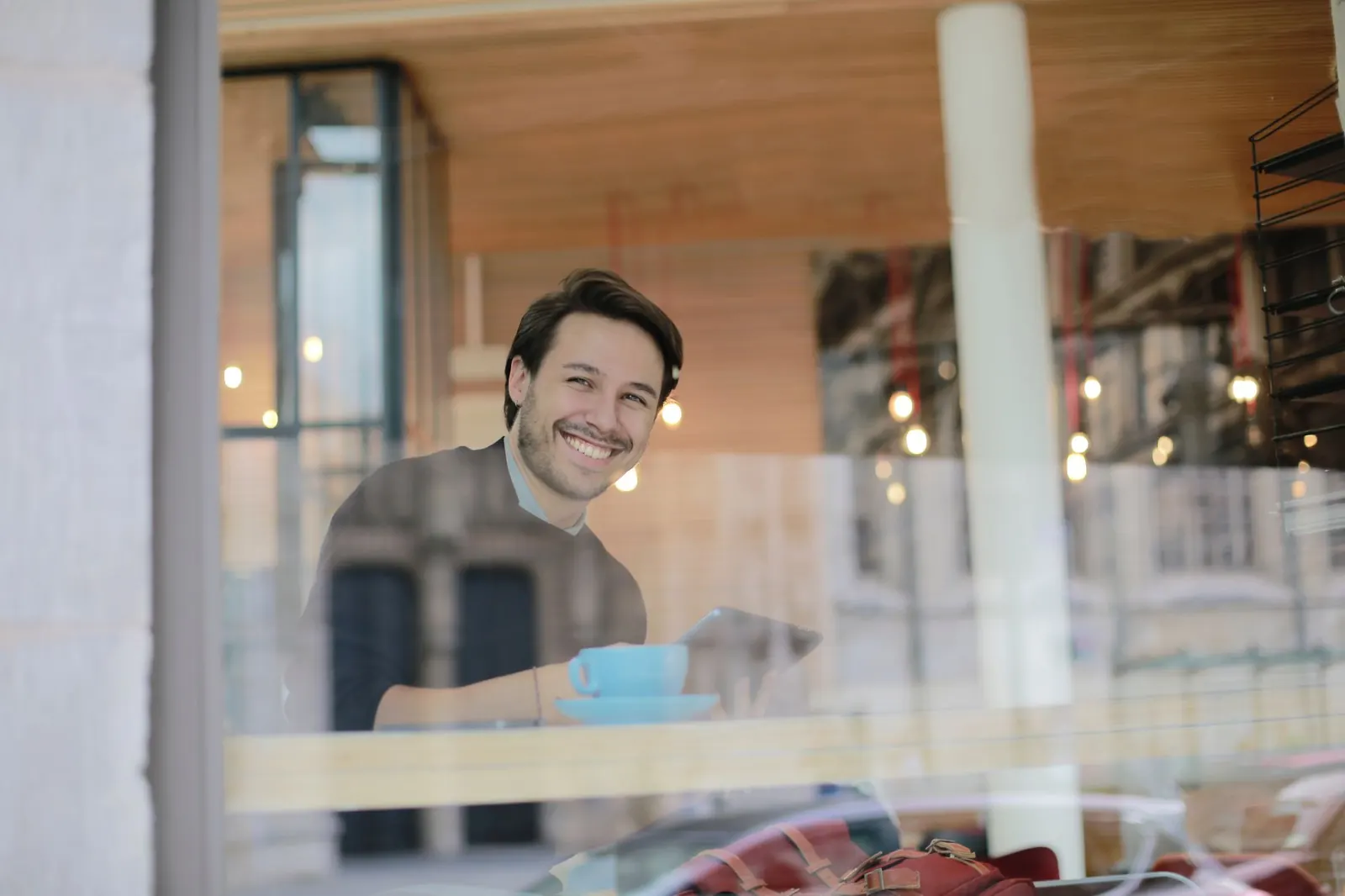 A smiling man with a coffee in a café, seen through the window