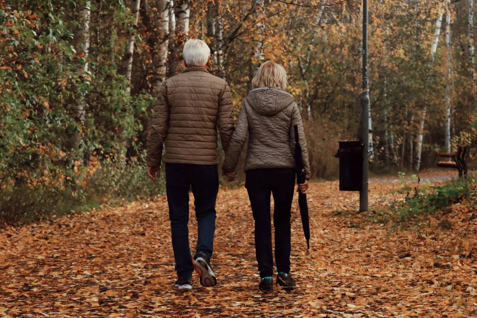 An older couple walking through a park in autumn