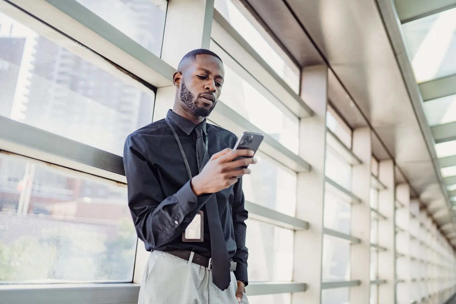 A professional checking his phone in a glass-walled office building