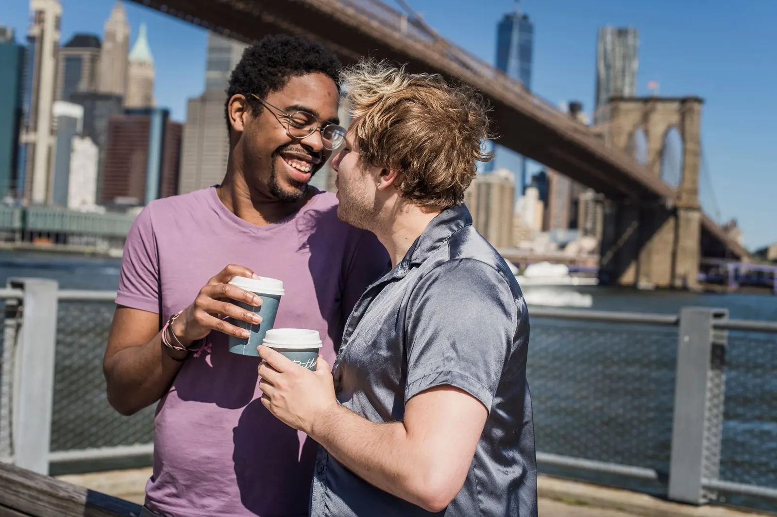 Two men laughing over coffee by the Brooklyn Bridge