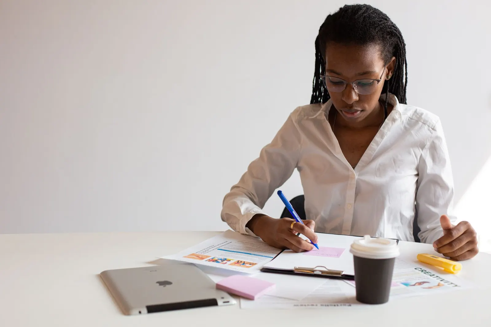 A woman taking notes at a desk with papers and a coffee