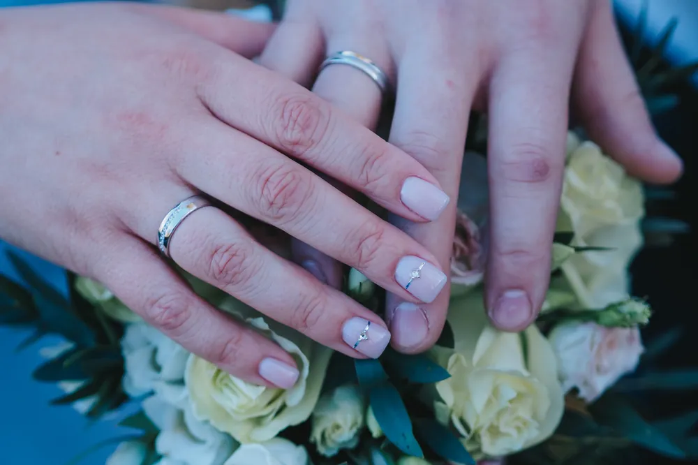 Two hands with wedding rings resting on a bouquet