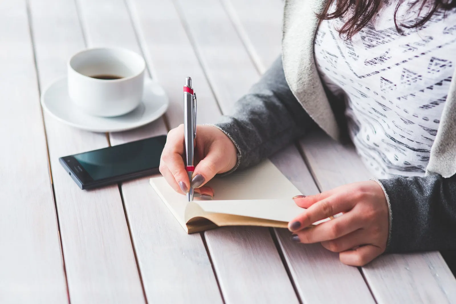 A woman writing in a journal next to a cup of coffee