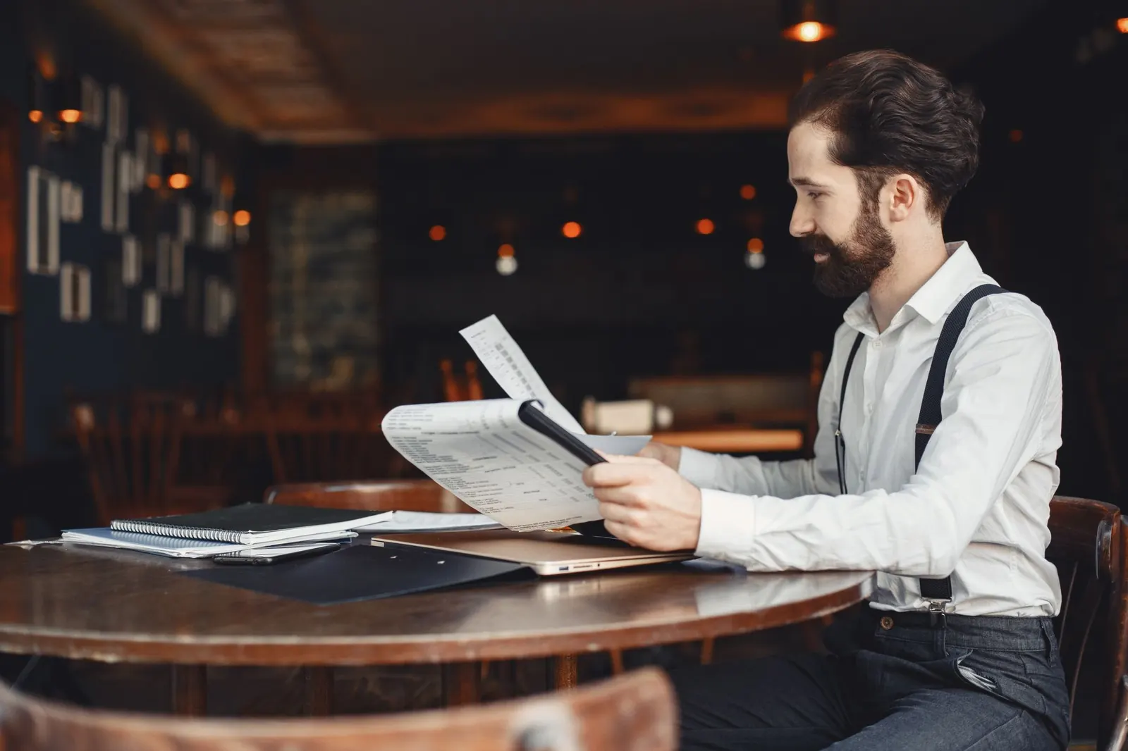 A man reading a printed page at a wooden café table