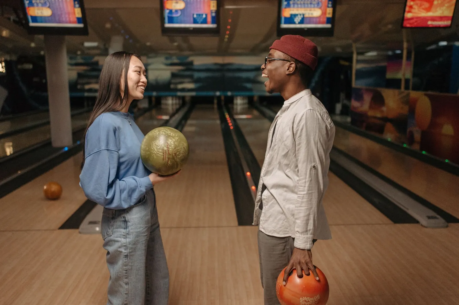Two people talking with bowling balls in hand at a bowling alley