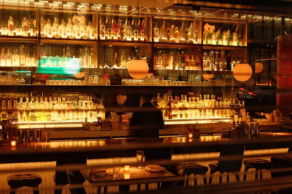 A warmly lit bar in New York with shelves of bottles