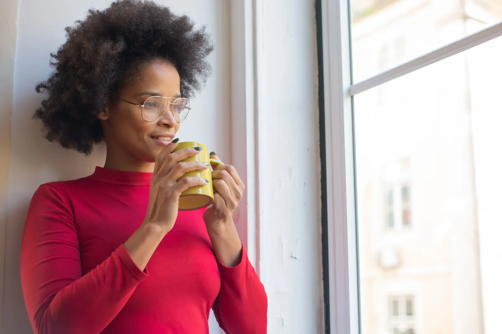A woman holding a cup and looking out of a window